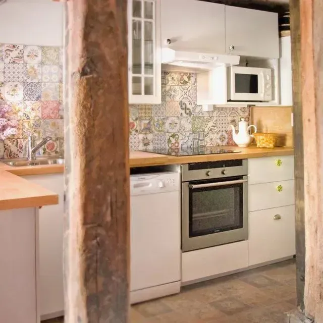 Cocina con gabinetes blancos, salpicadero de azulejos de colores, encimera de madera y horno.