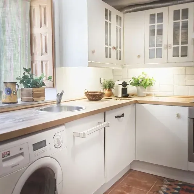 Cocina blanca con encimera de madera, ventana, lavadora.