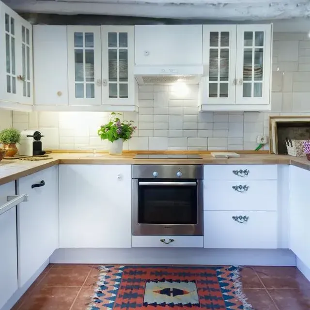 Cocina blanca con encimeras de madera, horno de acero inoxidable y alfombra colorida.
