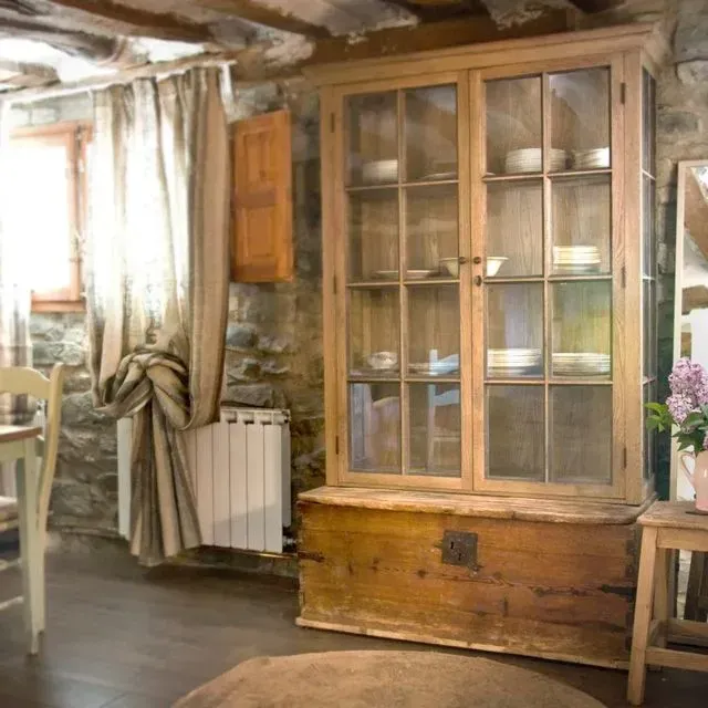 Un armario de madera con puertas de cristal se encuentra sobre un antiguo arcón de madera en una habitación rústica.