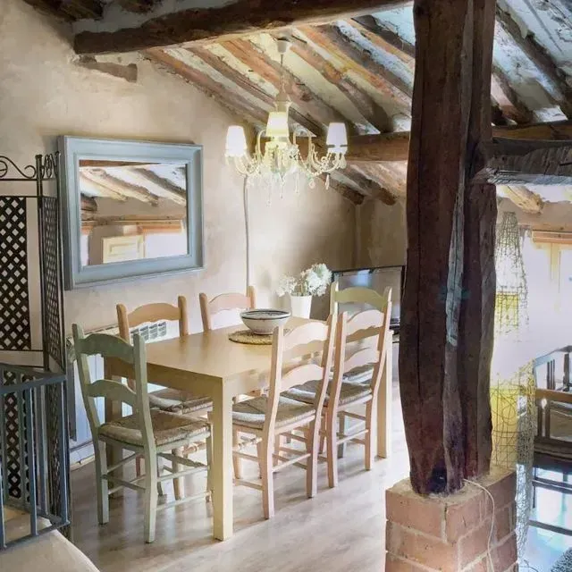 Comedor con mesa de madera, sillas, espejo y lámpara de araña. Decoración rústica con vigas vistas.