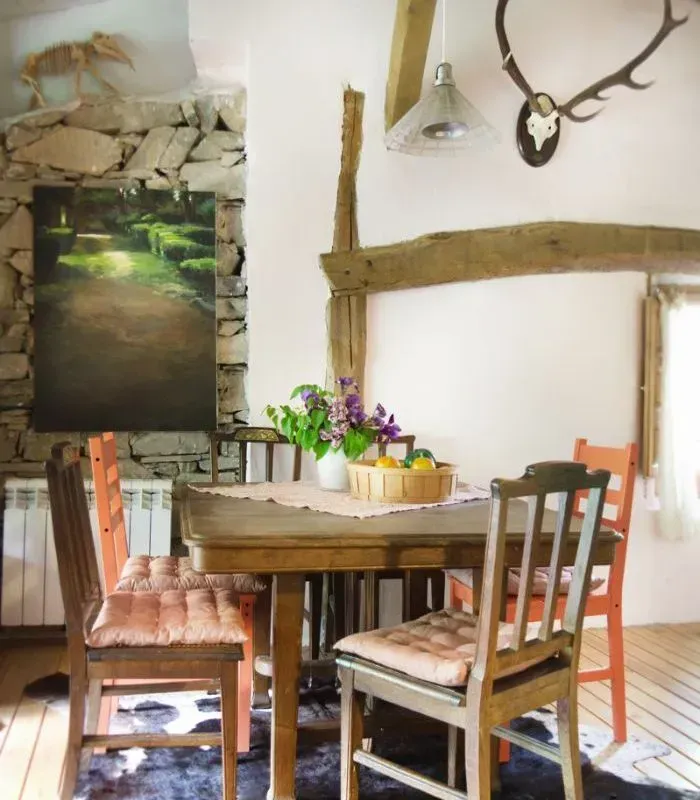 Comedor con pared de piedra rústica, mesa de madera, sillas de colores, decoración de astas.