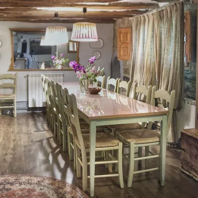 Comedor rústico con mesa larga para muchos, sillas verde suave, pisos de madera, centro de mesa floral.