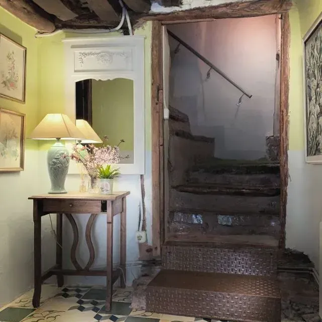 Pasillo con escalera, mesa, espejo, cuadro y suelo con estampado verde y azul. Vigas y molduras de madera.