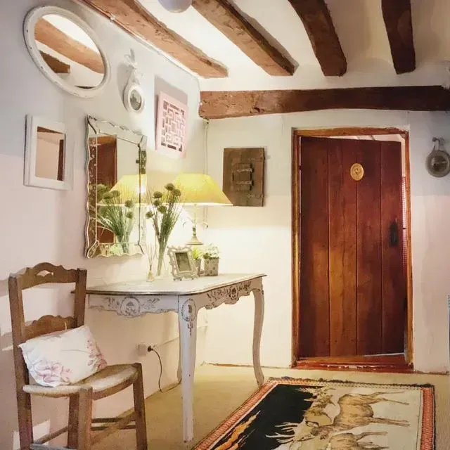 Acogedora habitación con vigas de madera, una pequeña mesa, espejo y puerta de madera.