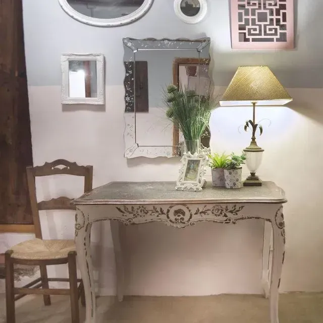 Un tocador rústico con silla, lámpara, espejos y decoración contra una pared de dos tonos.