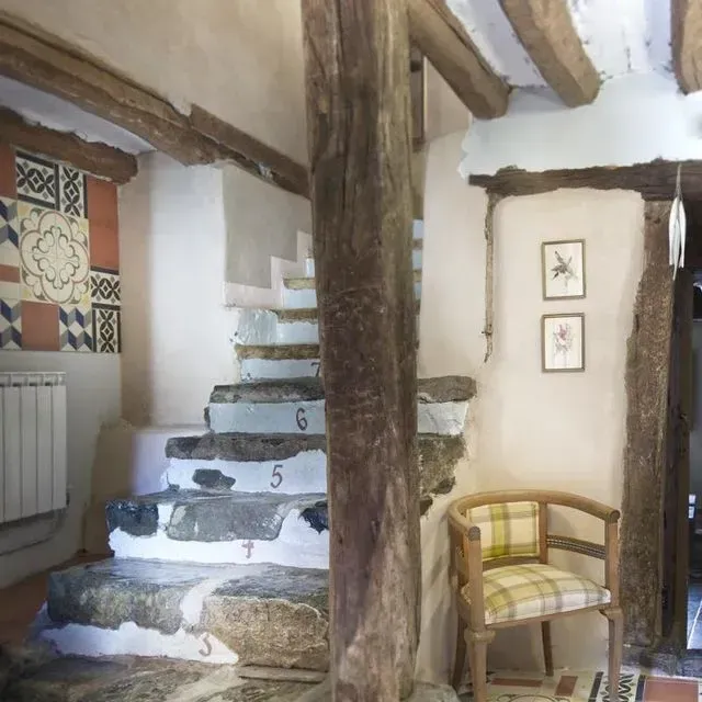 Escalones de piedra en un interior rústico, vigas de madera, silla con cojín a cuadros, diseño de pared de azulejos.