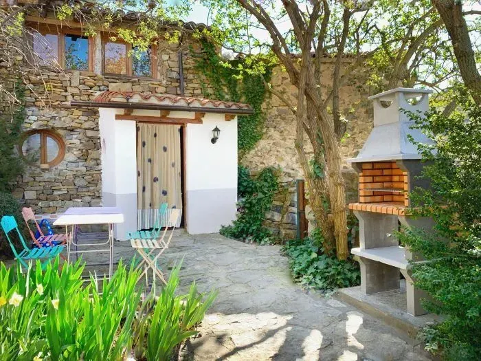 Casa de piedra con zona de estar al aire libre, barbacoa y vegetación.