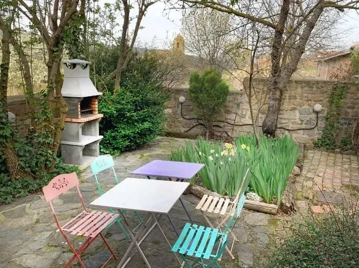 Patio exterior con mesas y sillas de colores, barbacoa de piedra y jardín.