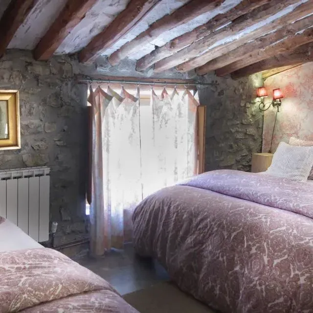 Dormitorio con paredes de piedra, vigas de madera y dos camas individuales con ropa de cama de paisley rosa.