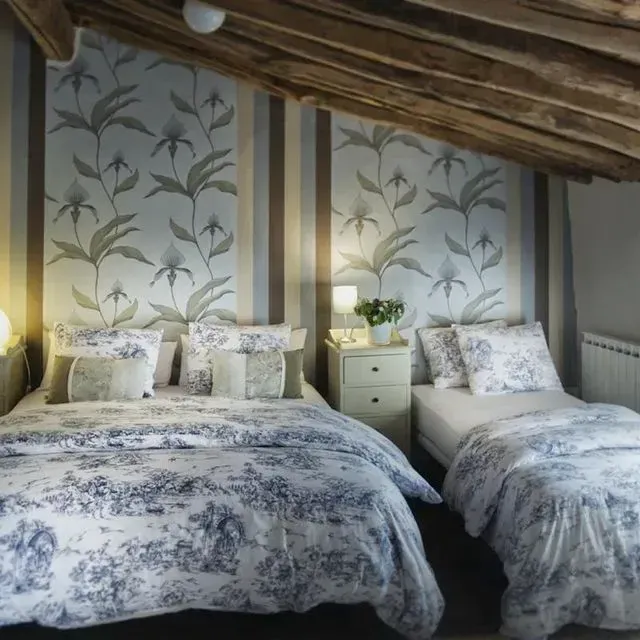 Dormitorio con cama doble, cama individual, papel pintado floral y techo con vigas de madera.