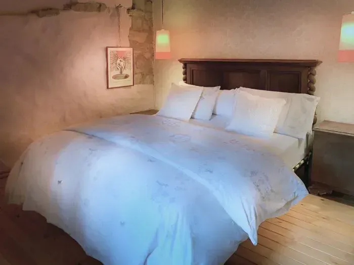 Dormitorio con cama grande, sábanas blancas, cabecero de madera, dos lámparas colgantes y un cuadro enmarcado en la pared.