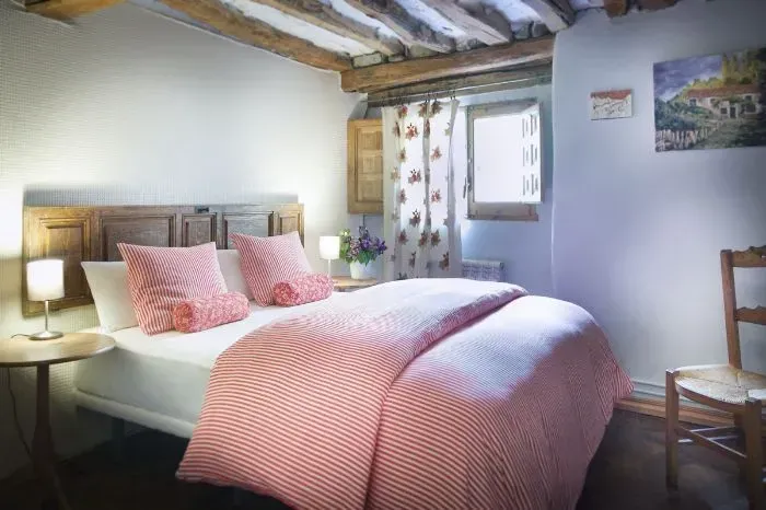 Dormitorio con cama tapizada de cuadros vichy rojos, cortinas florales, vigas de madera y un pequeño cuadro.