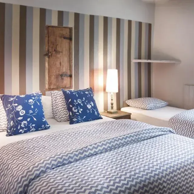 Dormitorio con pared rayada, cama, almohadas con estampados azules, cama individual pequeña y puerta de madera.