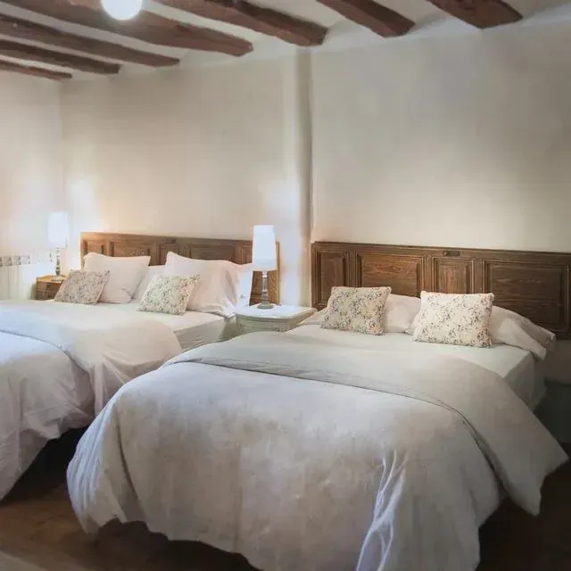 Dormitorio con dos camas, sábanas blancas, cabeceros de madera y vigas rústicas en el techo.