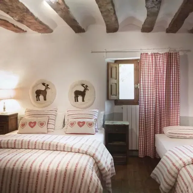Dormitorio con dos camas, ropa de cama de rayas rojas, arte de ciervos, cortinas a cuadros rojos, vigas de madera.