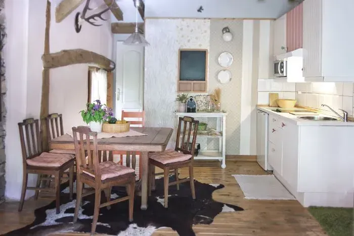 Acogedora cocina con mesa de comedor y sillas sobre una alfombra de piel de vaca, con una pequeña zona de cocina.