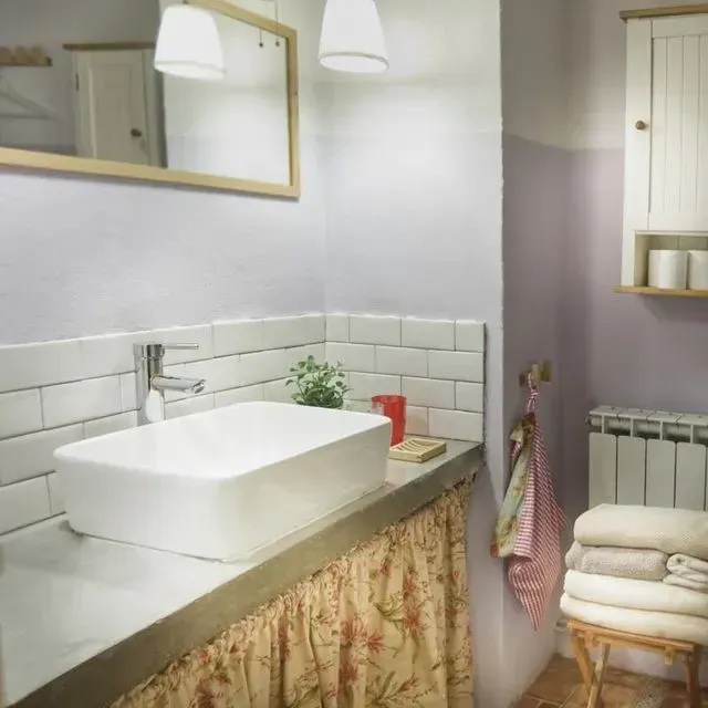 Baño con lavabo rectangular blanco, cortina floral y toallas apiladas.