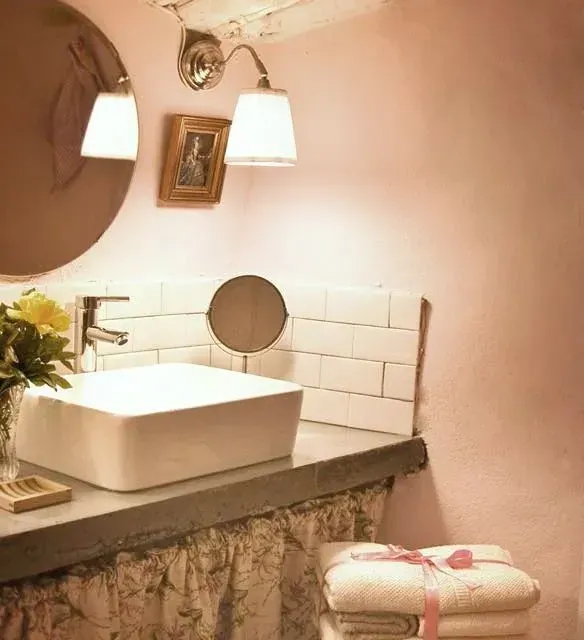 Baño rosa con lavabo blanco, espejo redondo y un pequeño cuadro enmarcado.
