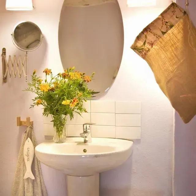 Baño con lavabo redondo, espejo ovalado, flores amarillas y toallero decorativo con forma de pez.