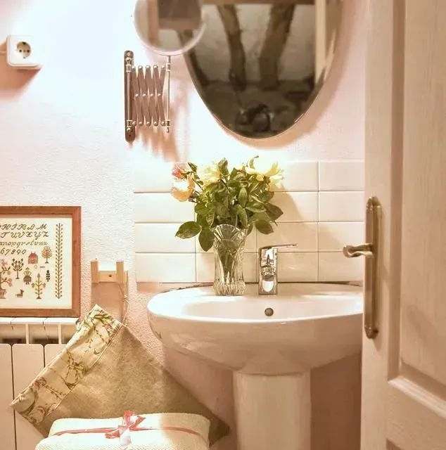 Baño pequeño con lavabo de pedestal, flores y espejo. Paredes rosas.