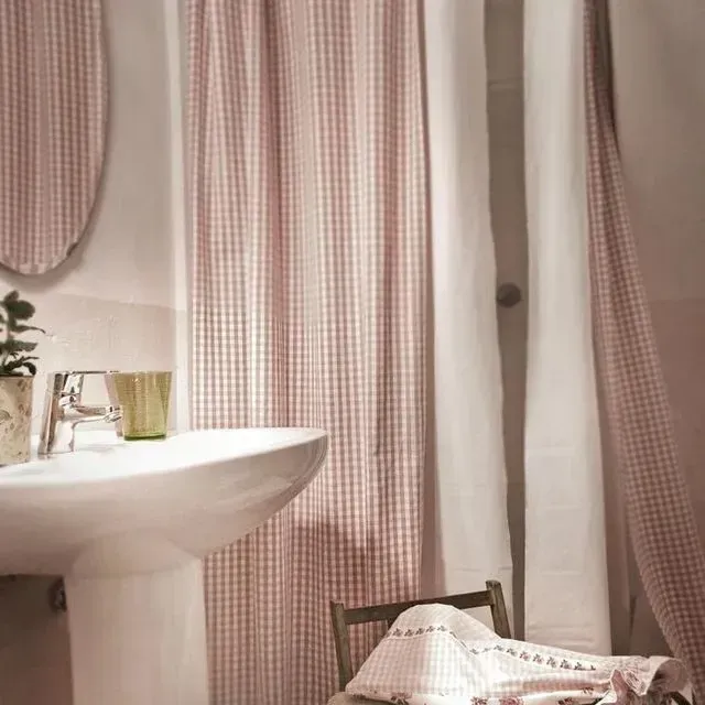 Un baño de temática rosa con lavabo con pedestal, cortina de ducha estampada, espejo y silla con toalla.