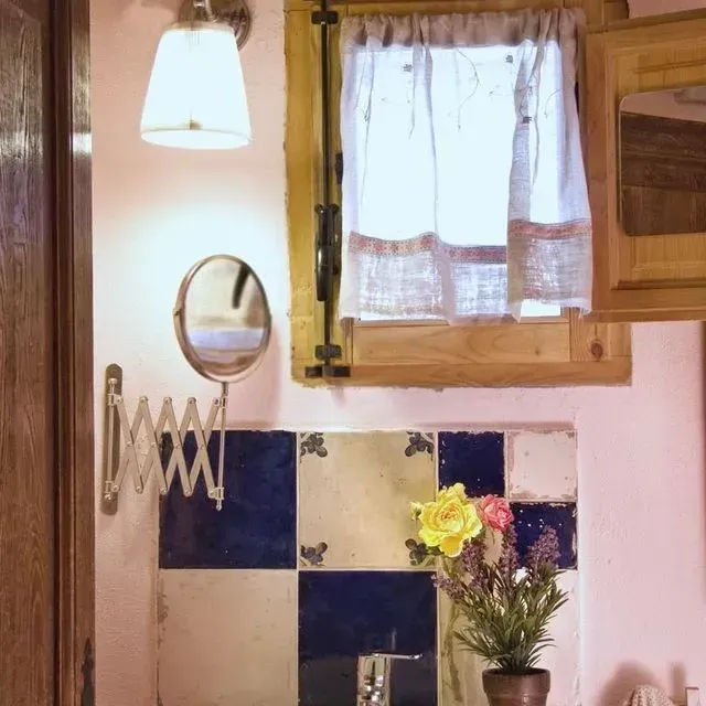 Baño pequeño con salpicadero de azulejos azules y blancos, una ventana con cortina y un espejo de pared.