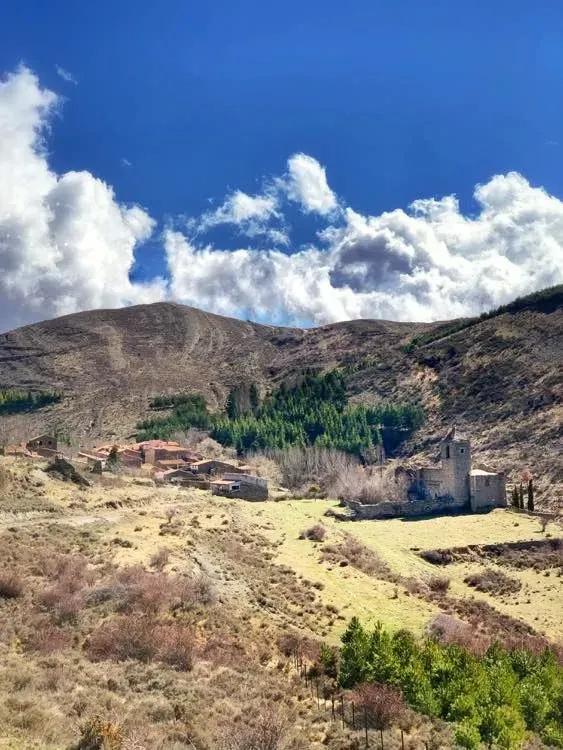 Hay una casa en medio de un campo con montañas al fondo.
