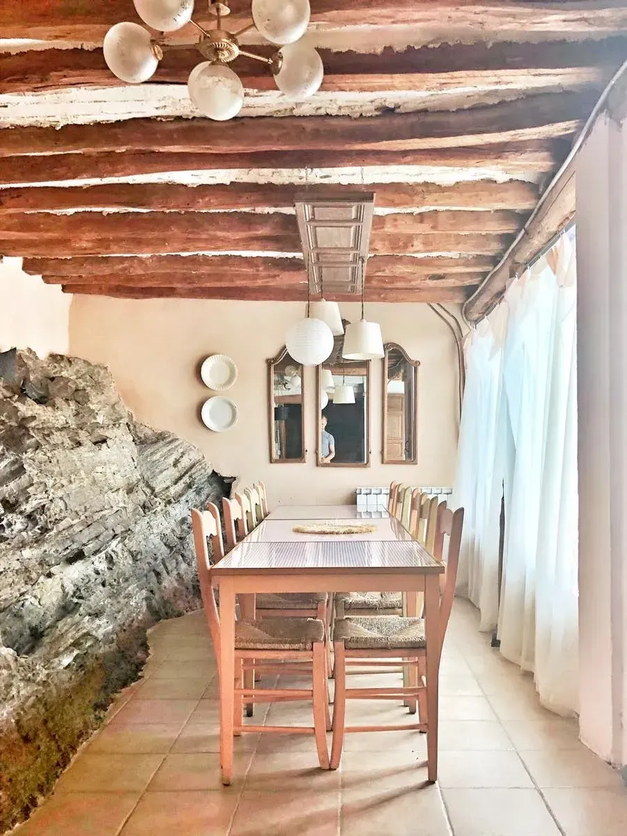 Comedor con mesa larga de madera, pared de roca, techo con vigas de madera, espejos y sillas.