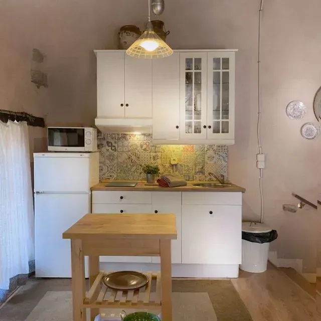 Cocina pequeña y blanca con encimera de madera, microondas e isla; el protector contra salpicaduras tiene azulejos estampados.