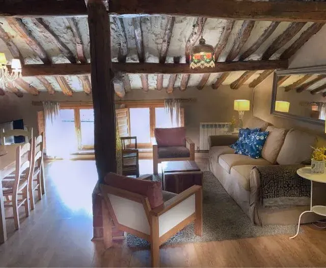 Acogedora sala de estar con vigas a la vista, un sofá, sillas y un comedor; entra mucha luz natural.