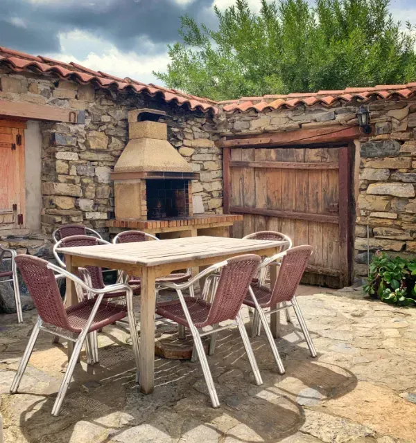 Comedor en patio con paredes de piedra, techo de ladrillo, parrilla y mesa con sillas.