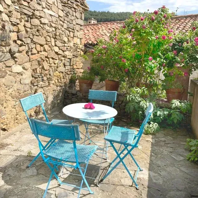 Un pintoresco patio con mesa y sillas turquesas, muro de piedra y rosales.