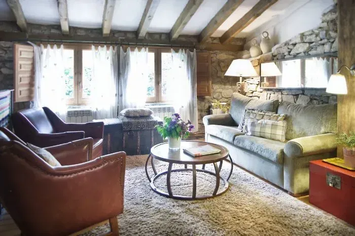 Acogedora sala de estar con paredes de piedra, vigas de madera, sillas de cuero, sofá y una mesa de café.