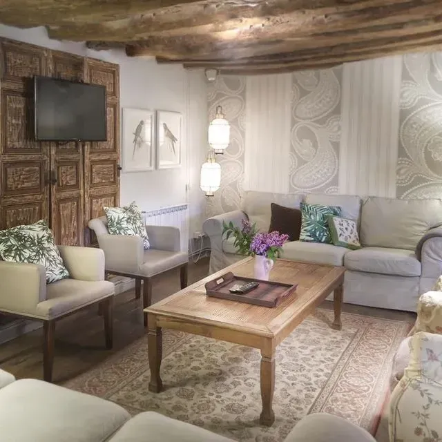 Sala de estar con sofá, sillas, mesa de madera y panel de puerta ornamentado, colores neutros.