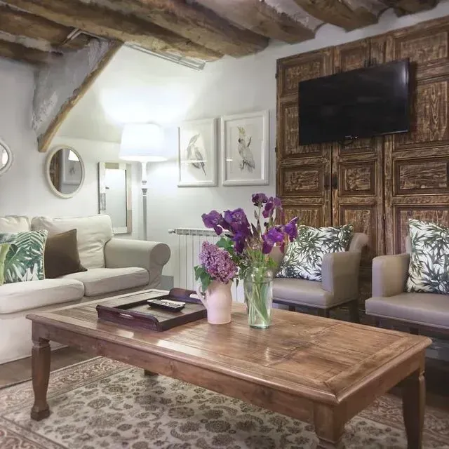 Acogedora sala de estar con techo de madera, decoración floral y TV montada sobre paneles rústicos.