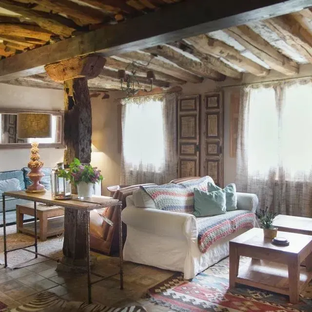 Acogedora sala de estar rústica con techo con vigas de madera, sofá y muebles de estilo antiguo.