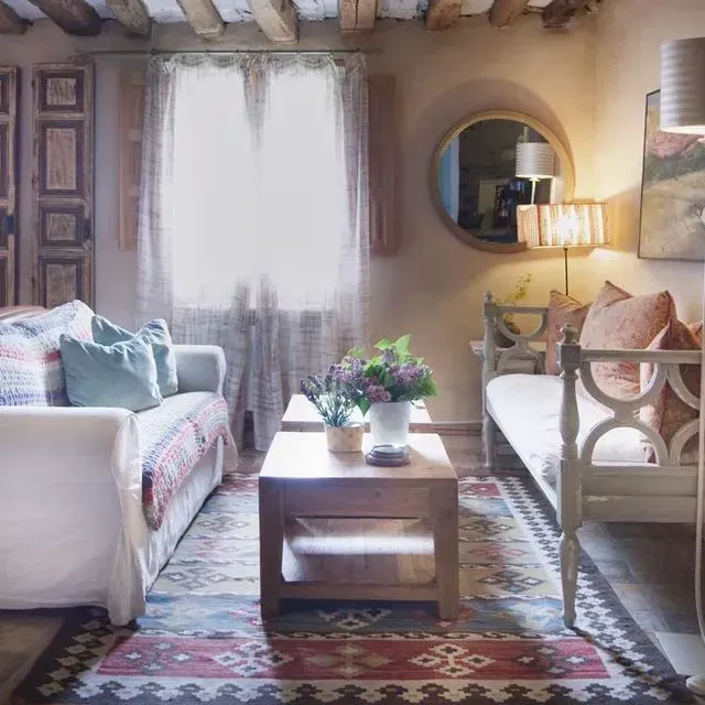 Acogedora sala de estar con sofá, diván, alfombra y vigas de madera; tonos neutros y una ventana.