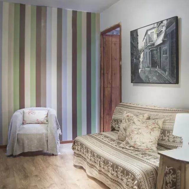 Una habitación con una pared rayada, un sofá con funda estampada, un sillón y un cuadro en la pared.