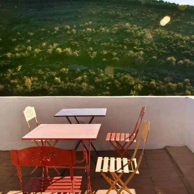 Mesas y sillas de exterior coloridas en una terraza con vistas a una ladera verde.