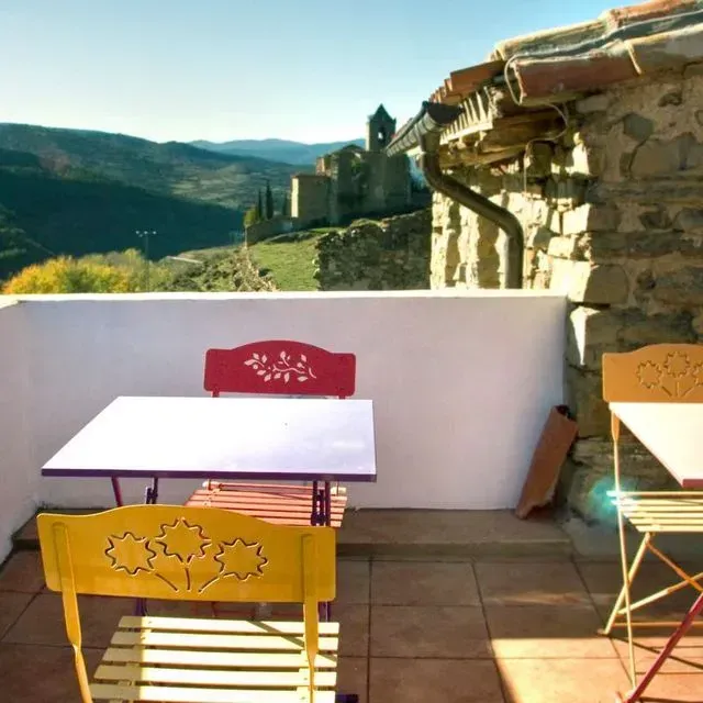 Patio al aire libre con sillas y mesas de colores, con vistas a un valle verde y al pueblo.
