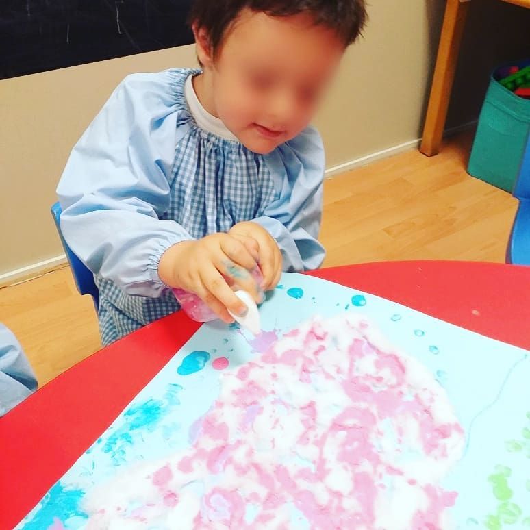 Un niño está sentado en una mesa jugando con pintura de espuma.