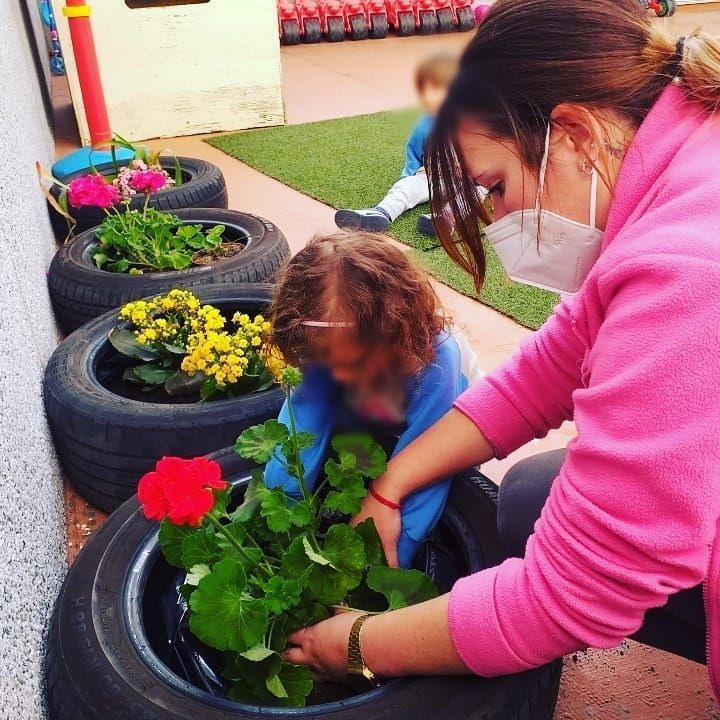 Una mujer con una máscara está plantando flores en un neumático.
