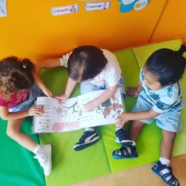 Tres niños están sentados en una alfombra verde leyendo un libro.