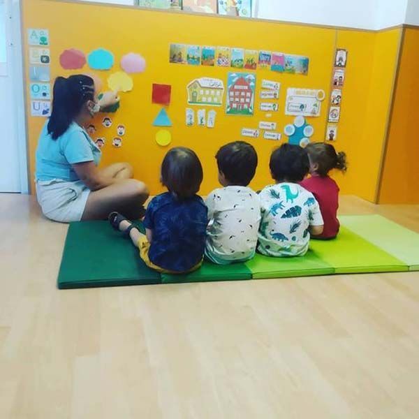 Un grupo de niños está sentado en una estera frente a una pared amarilla.