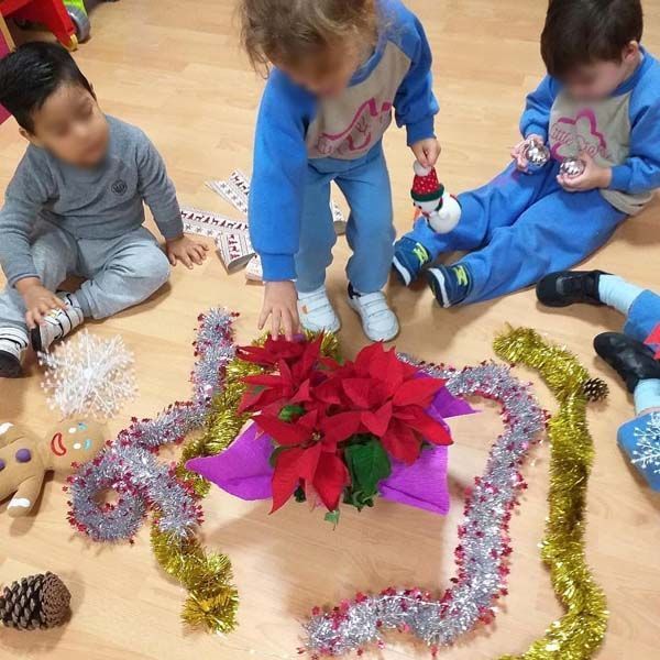 Tres niños están sentados en el suelo jugando con adornos navideños.
