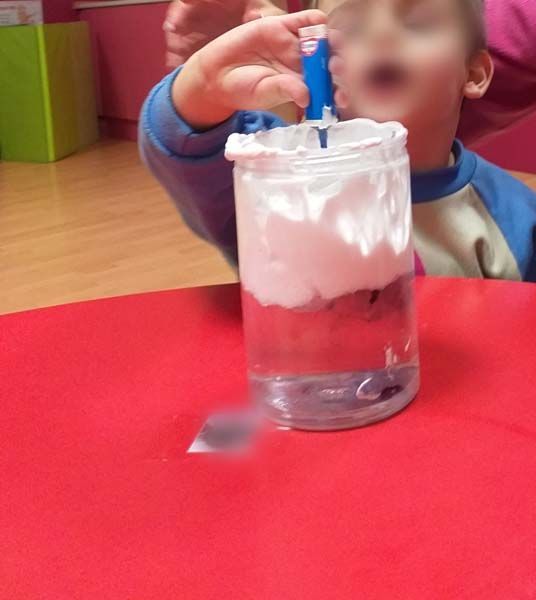 Un niño está jugando con un vaso de agua y bolitas de algodón.