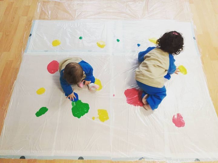 Dos niños están jugando con pintura sobre una lámina de plástico.