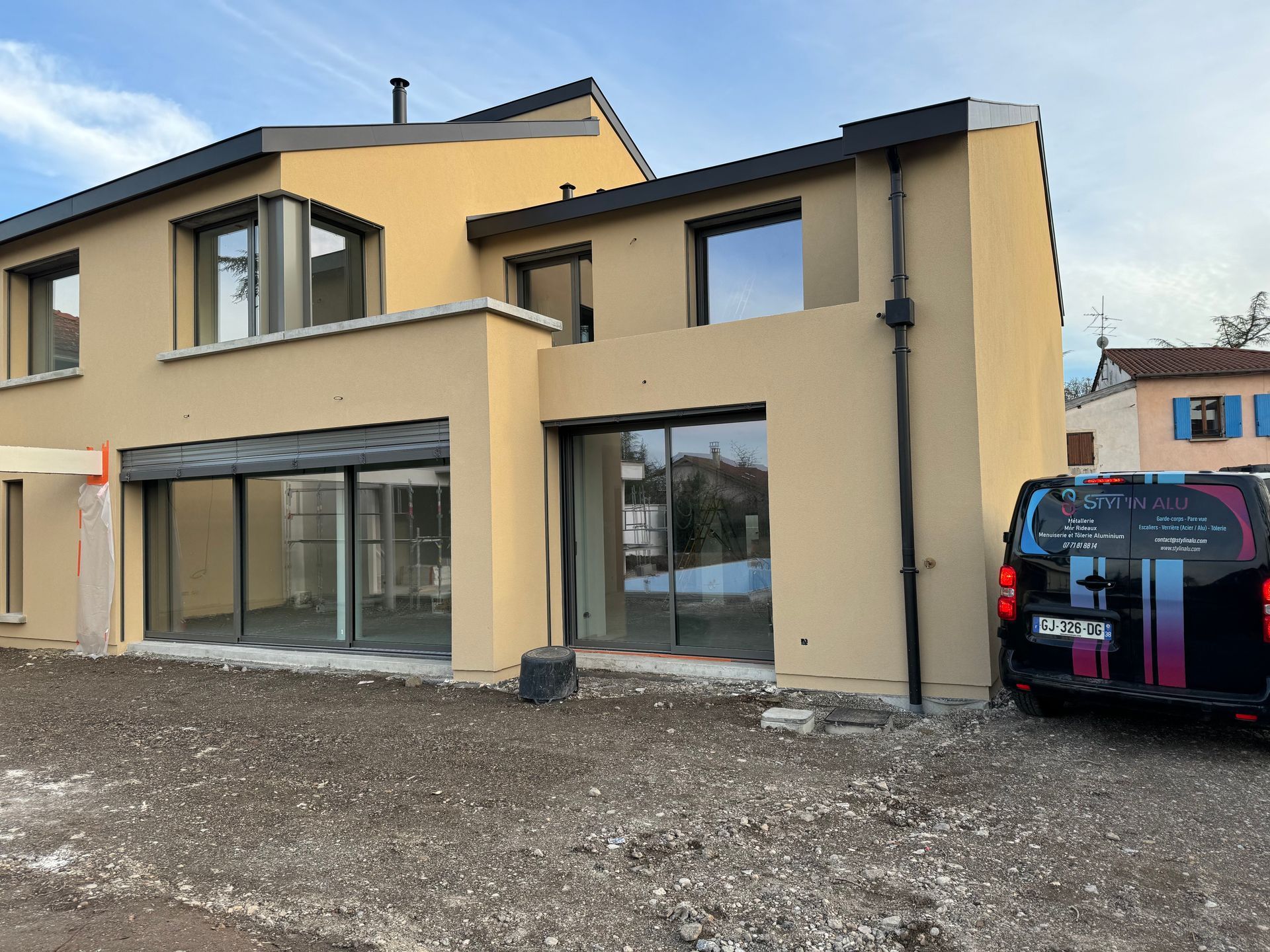 Maison moderne à deux étages avec de grandes fenêtres, façade en stuc beige et camionnette de service garée.
