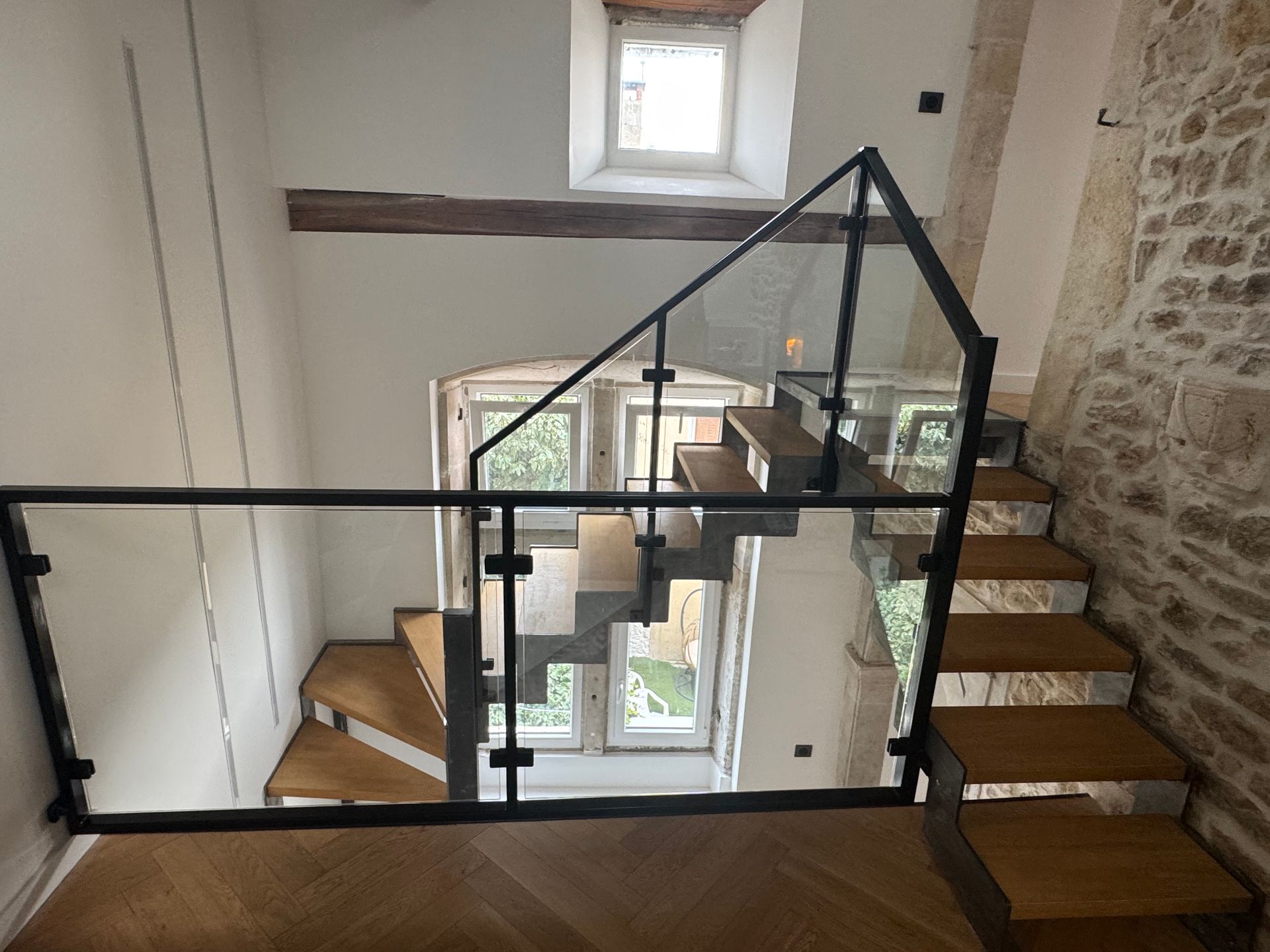 Escalier en bois avec rambarde en verre dans un bâtiment en pierre.